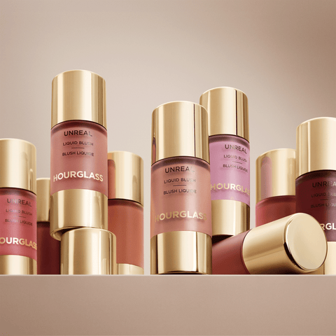 Hourglass Liquid Blush in a row of gold and clear bottles showing shades of pink, mauve, and terracotta on a beige background.